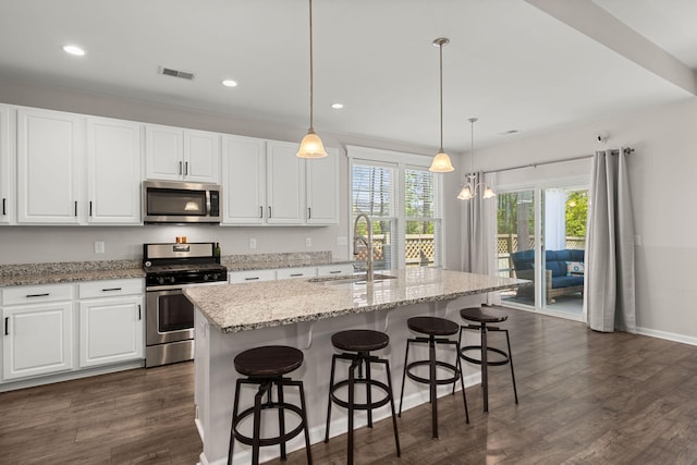 kitchen featuring sink, stainless steel appliances, white cabinets, a center island with sink, and decorative light fixtures