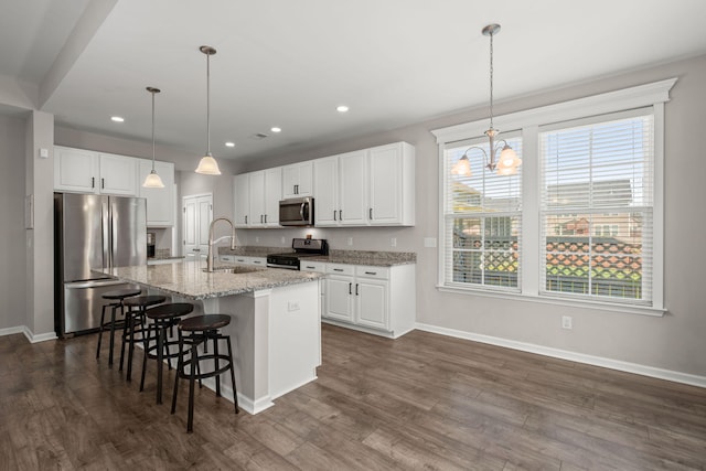 kitchen featuring sink, appliances with stainless steel finishes, white cabinetry, a kitchen island with sink, and light stone counters