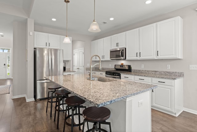 kitchen featuring appliances with stainless steel finishes, light stone countertops, a kitchen island with sink, and white cabinets