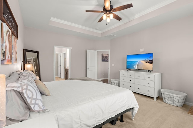 carpeted bedroom with ornamental molding, ensuite bath, ceiling fan, and a tray ceiling