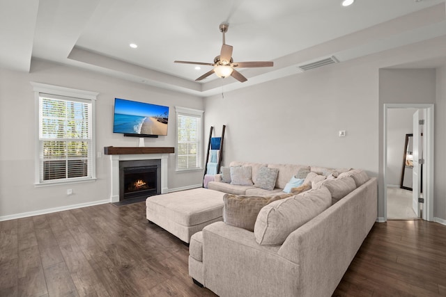 living room with dark hardwood / wood-style floors, ceiling fan, and a tray ceiling