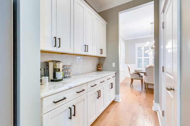 bar featuring a chandelier, light wood-style flooring, baseboards, ornamental molding, and tasteful backsplash