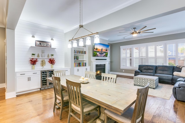 dining room featuring light wood-style flooring, beverage cooler, plenty of natural light, and a lit fireplace