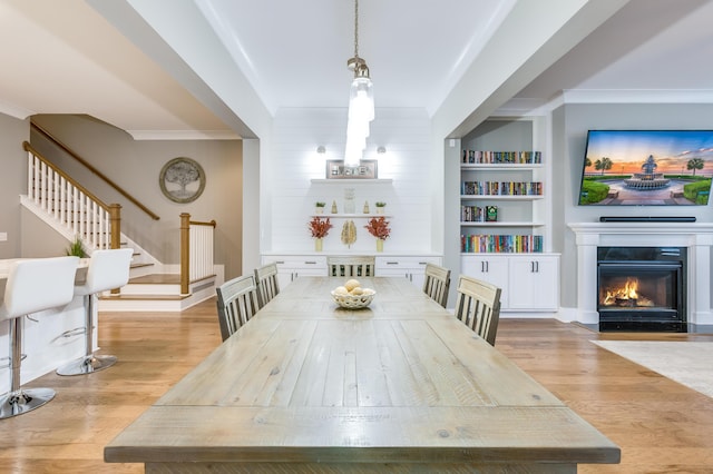 dining area with light wood-style floors, built in features, a fireplace with flush hearth, and stairs