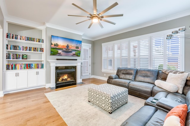 living area with ceiling fan, light wood-style flooring, a fireplace with flush hearth, baseboards, and crown molding