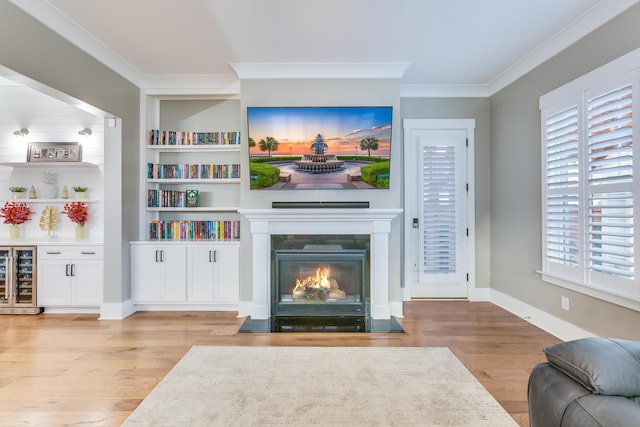 living area with beverage cooler, a fireplace with flush hearth, built in features, ornamental molding, and light wood finished floors