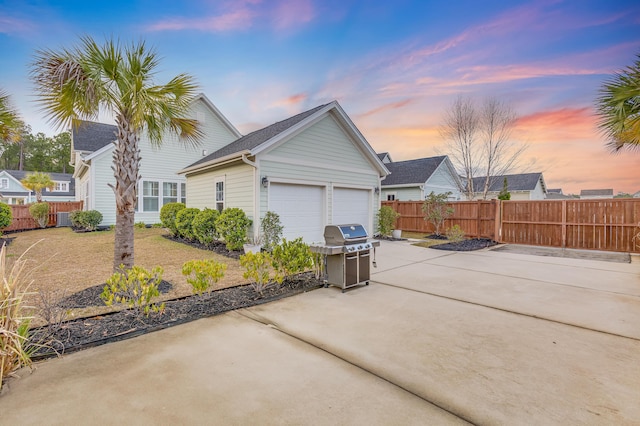 property exterior at dusk with driveway, an attached garage, and fence