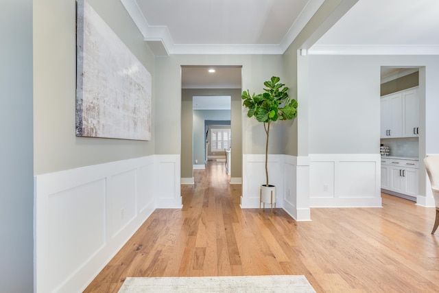 hall featuring light wood-style floors, ornamental molding, a decorative wall, and a wainscoted wall