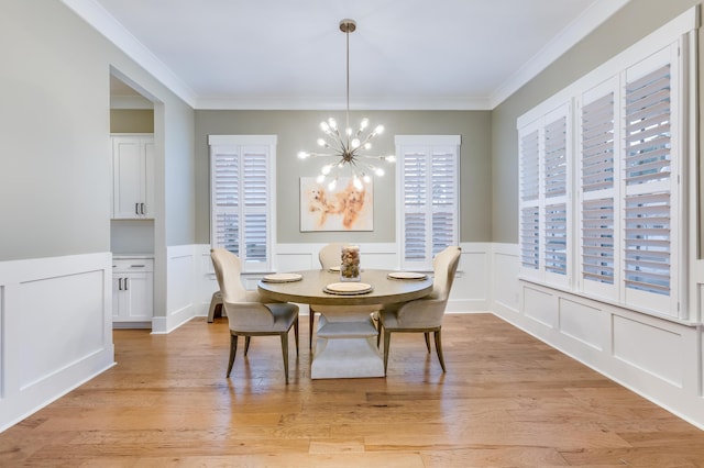 dining area with light wood-type flooring, crown molding, a notable chandelier, and wainscoting