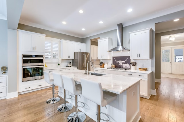 kitchen with tasteful backsplash, wall chimney exhaust hood, appliances with stainless steel finishes, a kitchen breakfast bar, and a sink