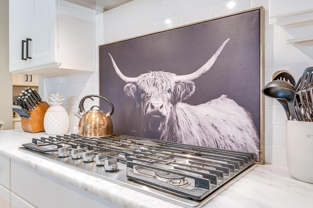 details with white cabinetry, tasteful backsplash, stainless steel gas cooktop, and light countertops