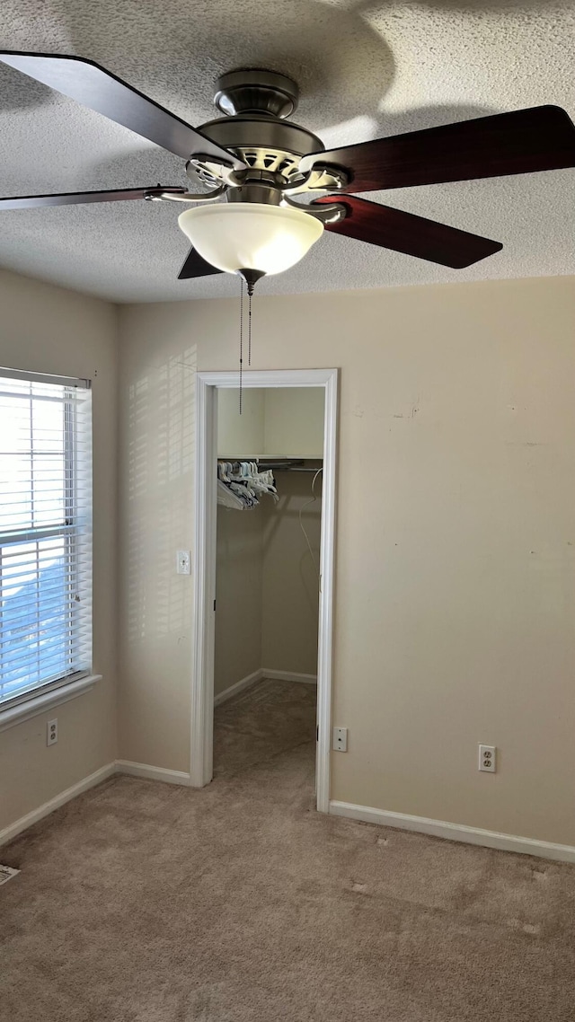 unfurnished bedroom with a ceiling fan, carpet, a textured ceiling, and a spacious closet