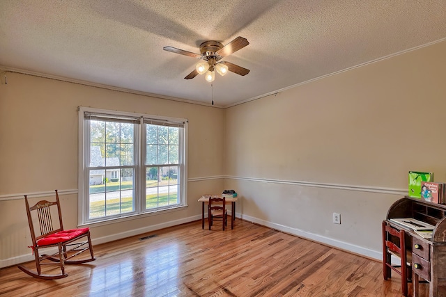 living area with a textured ceiling, light wood-style flooring, visible vents, baseboards, and a ceiling fan