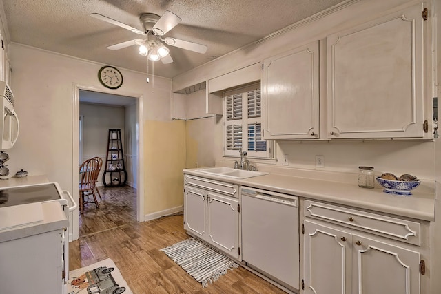 kitchen featuring a textured ceiling, white appliances, a sink, light countertops, and light wood finished floors