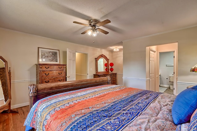 bedroom featuring a textured ceiling, wood finished floors, baseboards, ornamental molding, and ensuite bath