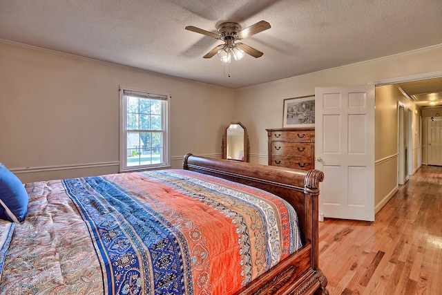 bedroom with a textured ceiling, a ceiling fan, light wood-style floors, ornamental molding, and attic access