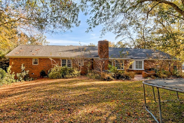 rear view of house featuring a chimney, crawl space, a trampoline, a yard, and brick siding