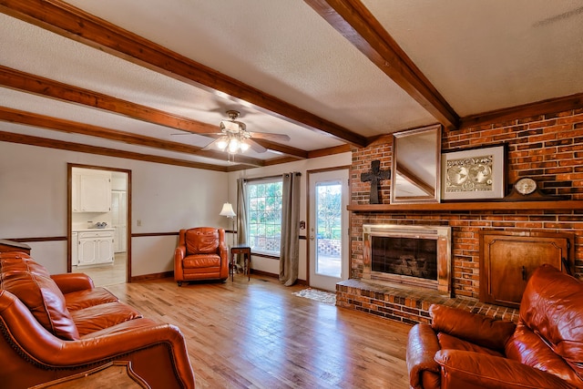 living room with beam ceiling, a brick fireplace, a textured ceiling, light wood-type flooring, and baseboards