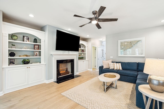 living room with ceiling fan, built in features, and light wood-type flooring