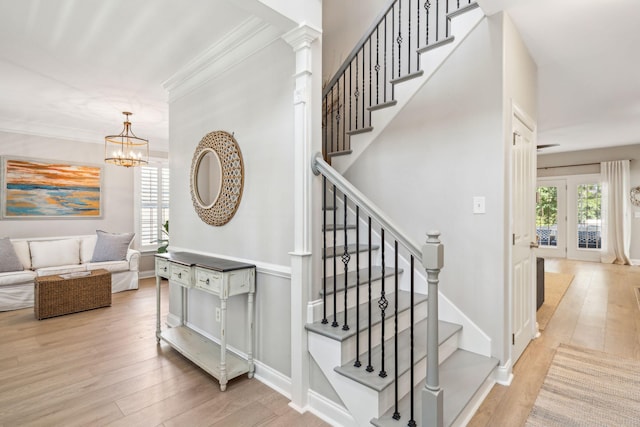 stairs featuring hardwood / wood-style flooring, ornamental molding, a chandelier, and a healthy amount of sunlight