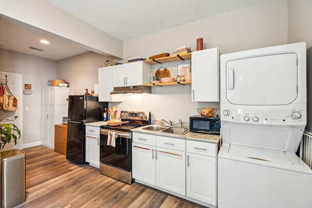 kitchen with stacked washer and dryer, black appliances, and white cabinets