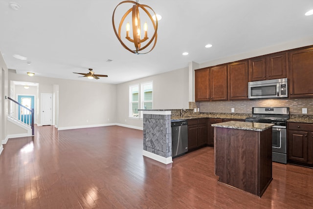 kitchen featuring kitchen peninsula, dark hardwood / wood-style flooring, tasteful backsplash, stainless steel appliances, and hanging light fixtures