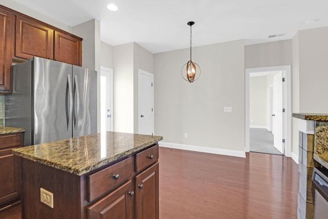 kitchen with pendant lighting, stone counters, stainless steel fridge, a kitchen island, and dark hardwood / wood-style flooring