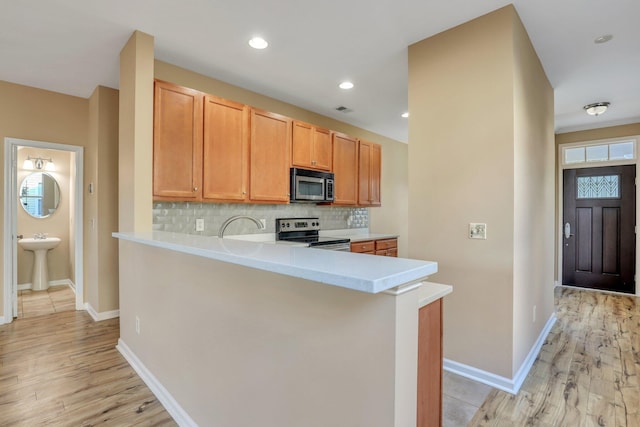 kitchen with kitchen peninsula, sink, appliances with stainless steel finishes, and light hardwood / wood-style flooring