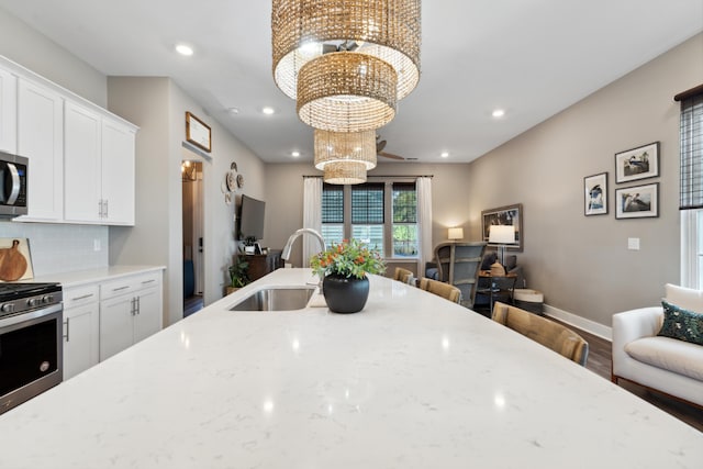 kitchen featuring white cabinetry, sink, stainless steel appliances, light stone counters, and a chandelier