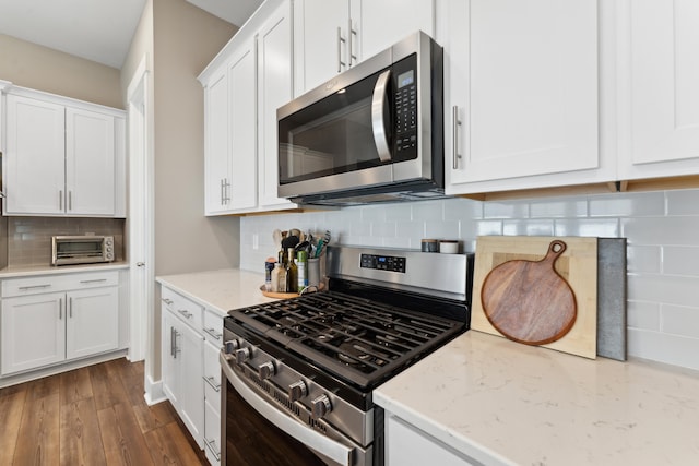 kitchen with appliances with stainless steel finishes, tasteful backsplash, light stone counters, dark wood-type flooring, and white cabinets