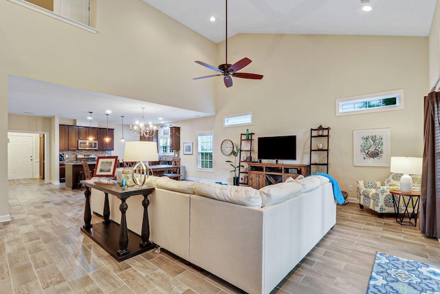 living room with high vaulted ceiling, light hardwood / wood-style floors, and ceiling fan with notable chandelier