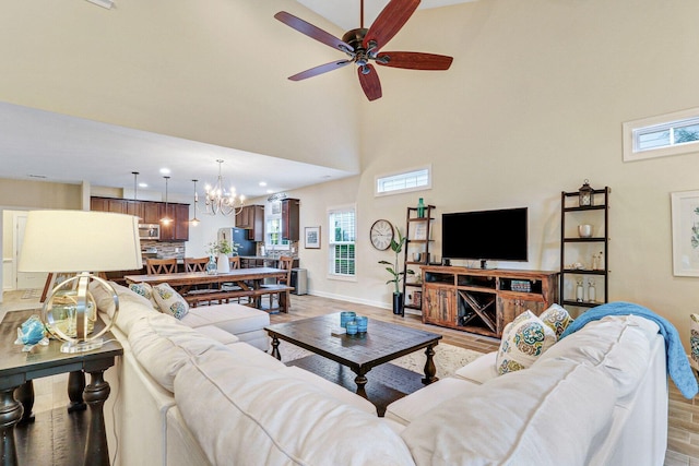 living room with a high ceiling, ceiling fan with notable chandelier, light hardwood / wood-style floors, and a healthy amount of sunlight