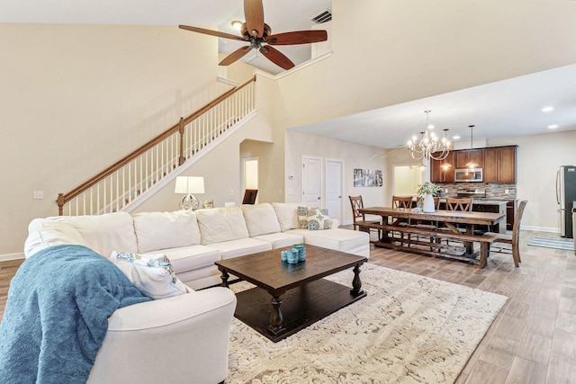 living room with ceiling fan with notable chandelier, light hardwood / wood-style floors, and high vaulted ceiling