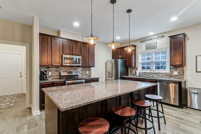 kitchen with appliances with stainless steel finishes, light hardwood / wood-style floors, light stone counters, a kitchen island, and decorative light fixtures