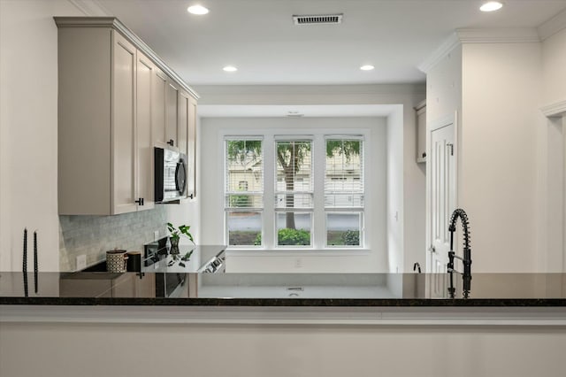 kitchen with dark stone countertops, recessed lighting, stainless steel microwave, decorative backsplash, and visible vents