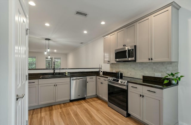 kitchen with visible vents, decorative backsplash, a sink, light wood-style flooring, and appliances with stainless steel finishes