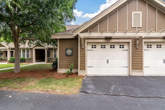 multi unit property with board and batten siding, driveway, roof with shingles, and a garage