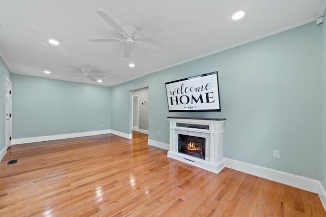 unfurnished living room featuring ceiling fan, light hardwood / wood-style flooring, a textured ceiling, and ornamental molding