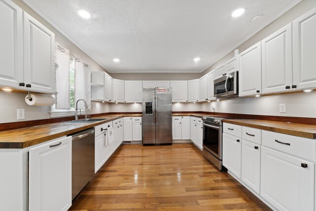 kitchen with white cabinetry, butcher block countertops, light wood-type flooring, stainless steel appliances, and sink