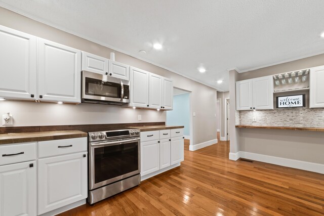 kitchen featuring appliances with stainless steel finishes, white cabinets, tasteful backsplash, ornamental molding, and light hardwood / wood-style floors