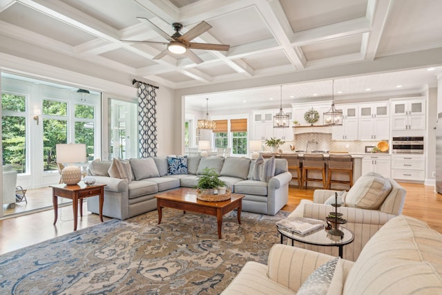 living room with ceiling fan, light hardwood / wood-style floors, beam ceiling, and coffered ceiling