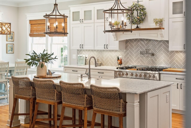 kitchen featuring a center island with sink, decorative backsplash, white cabinets, and light stone countertops