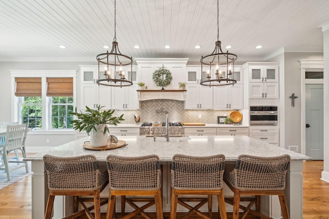 kitchen with stainless steel oven, crown molding, a kitchen bar, a kitchen island with sink, and white cabinets