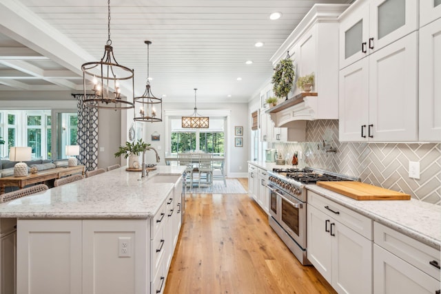 kitchen with hanging light fixtures, light stone counters, an island with sink, double oven range, and white cabinets