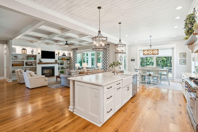 kitchen featuring white cabinets, a center island with sink, sink, hanging light fixtures, and light stone counters