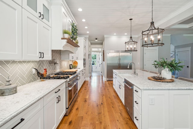 kitchen with light stone countertops, white cabinetry, decorative light fixtures, a kitchen island with sink, and appliances with stainless steel finishes