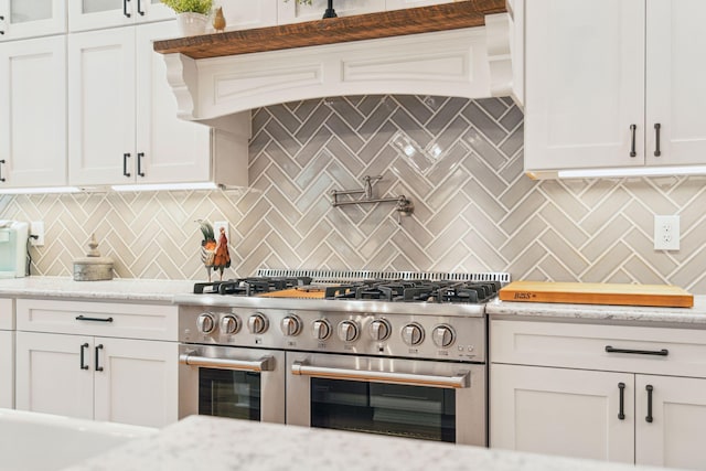 kitchen featuring white cabinets, range with two ovens, light stone countertops, and tasteful backsplash