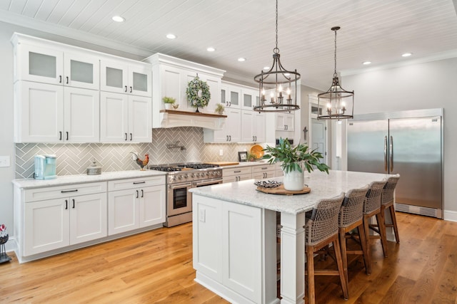 kitchen with light stone countertops, decorative light fixtures, high quality appliances, white cabinets, and a kitchen island