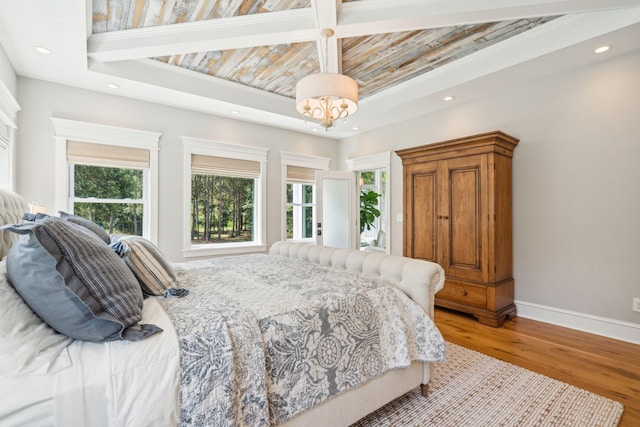 bedroom with a chandelier, a raised ceiling, wood-type flooring, and multiple windows