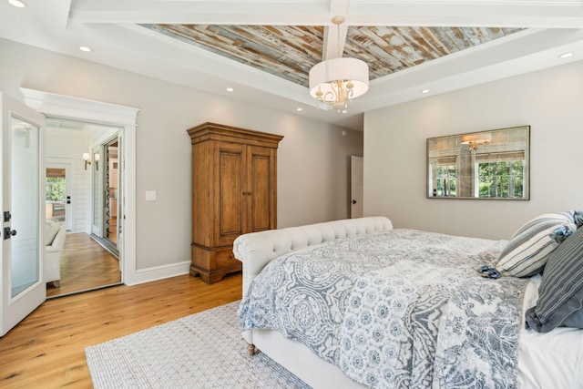 bedroom with a chandelier, multiple windows, a tray ceiling, and light hardwood / wood-style flooring